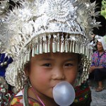 Small Asian girl in ceremonial headdress blowing bubble gum