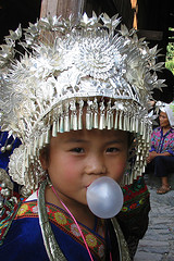 Small Asian girl in ceremonial headdress blowing bubble gum