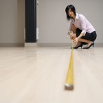 Young woman in large room, measuring floor with tape measure.