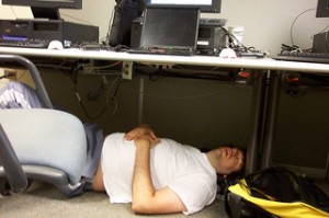 Man sleeping on the floor under a cubicle desk.