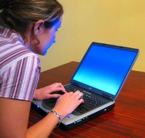 woman tyoing on laptop with head bent forward and shoulders hunched.
